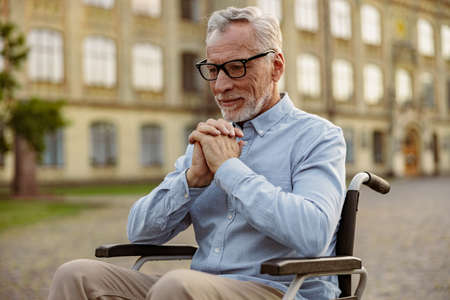 Portrait of pensive senior man handicapped patient in wheelchair looking thoughtful while spending time alone outdoors near rehabilitation clinicの写真素材