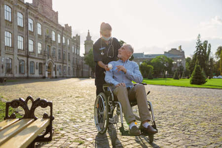 Focused senior man recovering patient listening to nurse advice, walking together outdoors near rehabilitation clinicの写真素材