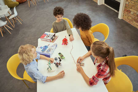 High angle view of diverse kids sitting at the table, examining technical toys full of details, spending time at engineering clubの写真素材