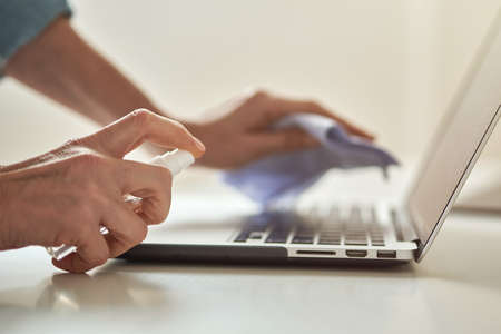 Close up shot of female hands using antibacterial sanitizer spray while disinfecting laptop keyboardの写真素材