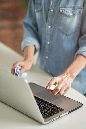 Close up shot of woman using antibacterial sanitizer spray while disinfecting her laptop and cleaning keyboardの写真素材