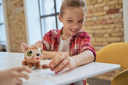 Charming little girl sitting at the table, examining technical toy and smiling, spending time at engineering clubの写真素材