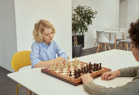 Think before you act. Thoughtful little caucasian boy playing chess with his friend, sitting together at the table in schoolの写真素材