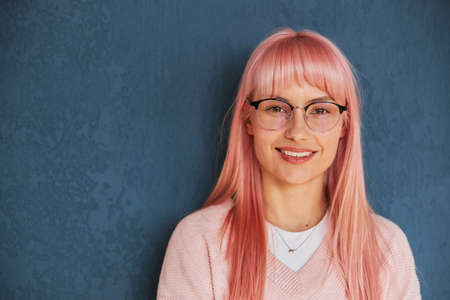 Pretty positive lady with glasses wearing stylish pullover stands near blue wallの写真素材