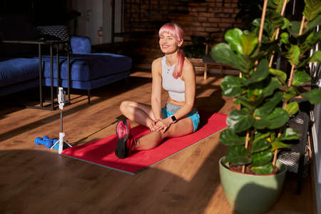 Happy woman in stylish top and shorts rests after training near mobile phone at homeの写真素材