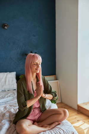 Calm woman with long pink hair meditates holding hand sin namaste on large bedの写真素材