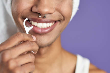 Close-up transgender man with dental floss smiling on purple background. Afroamerican trans genderの写真素材