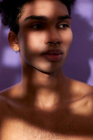 Verticale portrait of sensual young man in shadows. Sensitive hispanic model on purple backgroundの写真素材