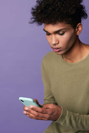 Portrait of brunette man with afro hairstyle using cellphone on purple backgroundの写真素材
