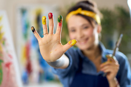 Cheerful woman smiling, creating abstract painting, applying colorful paints on canvas with fingers. Selective focus on hand in paintの写真素材