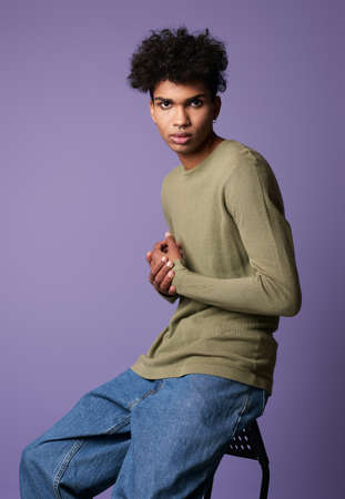 Portrait young transgender man sits in studio. Sexy male with black curly hairの写真素材