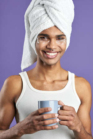 Young man with eye patches in towel on head and cup of tea portraitの写真素材