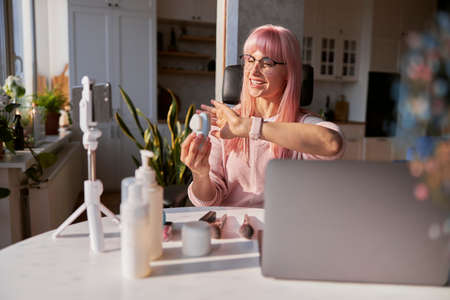 Positive lady with glasses presents electric facial cleansing brush shooting video at homeの写真素材