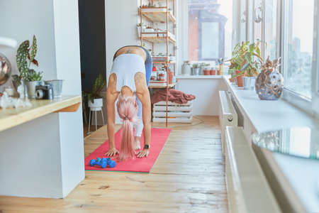 Slim pink haired woman with tattoo on back does forward bend at home trainingの写真素材