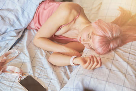 Tired woman with pink hair sleeps with mobile phone in comfortable bed at homeの写真素材