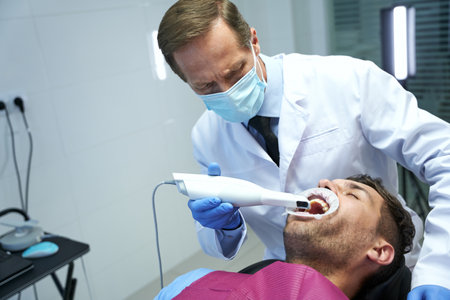 Serious doctor curing teeth of a male patientの写真素材