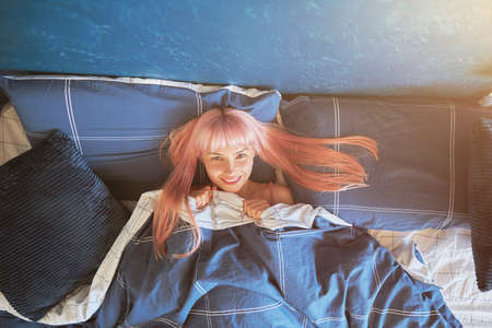 Cheerful lady lies under soft duvet in comfortable bed with soft pillowsの写真素材