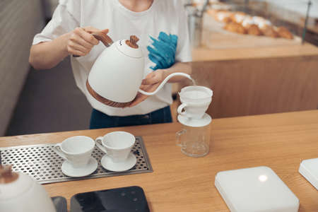 Female barista pouring boiled water through filter into glass mugの写真素材