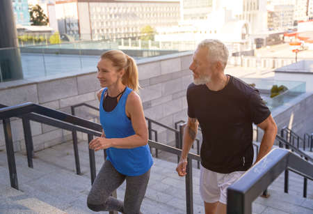 Active middle aged couple in sportswear running up a flight of stairs in city while working out together outdoorsの写真素材