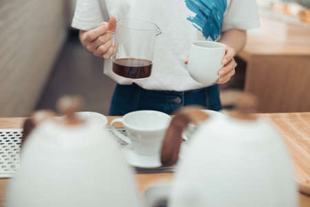 Female barista holding glass mug and cup of coffeeの写真素材