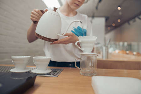Female barista pouring boiled water through filter into cupの写真素材
