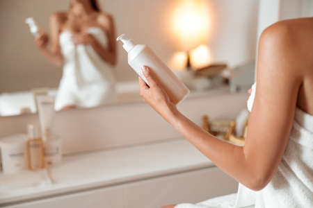 Young woman holding bottle of cosmetic cream or lotionの写真素材
