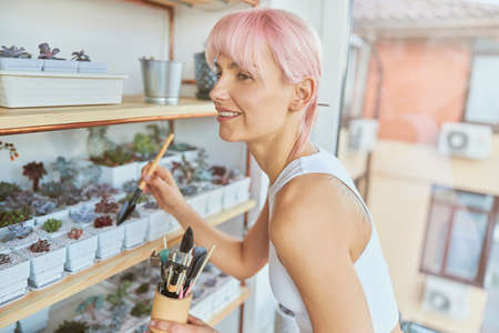 Cheerful female person takes care of exotic houseplants on light balconyの写真素材