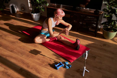 Pink haired woman checks time on smartwatch at training on floorの写真素材