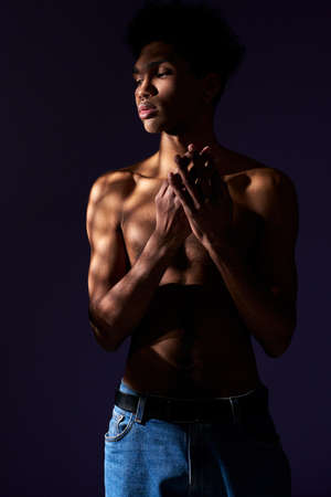 Portrait of transgender hispanic model with naked torso. Trans gender young man standing in shadowの写真素材