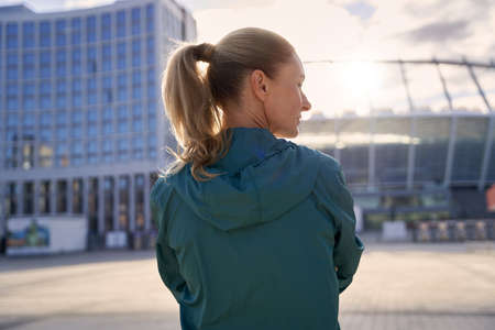 Rear view of sportive middle aged woman in sportswear standing outdoors, ready for morning workoutの写真素材
