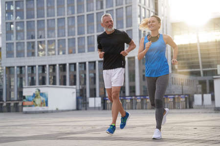 City running middle aged couple jogging together in the morning while training outdoorsの写真素材