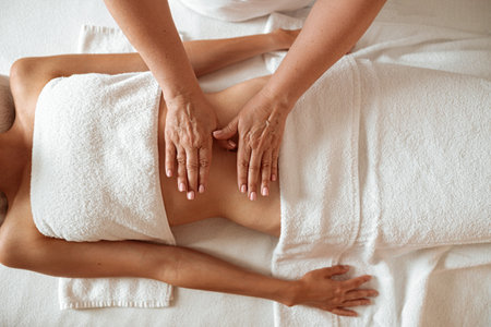 Slim young woman receiving stomach massage in spa salonの写真素材