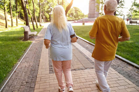 Healthy senior people in sports clothes run along green parkの写真素材