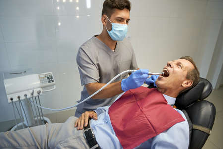 Male dentist doing treatment for man in chairの写真素材