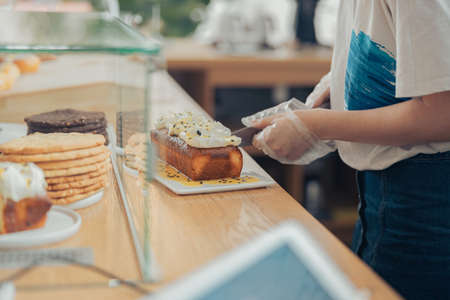 Young woman cutting cake in bakery shopの写真素材