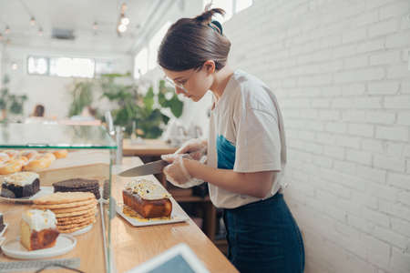 Beautiful young woman cutting cake in bakery shopの写真素材