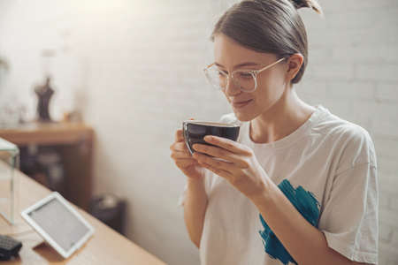 Charming young woman drinking coffee in cafeteriaの写真素材