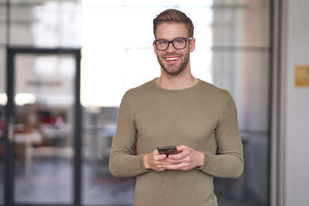 Businessman in glasses holding cellphone and waiting for ringの写真素材