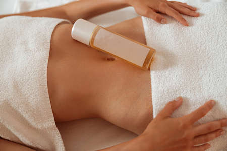Young woman with cosmetic product on her belly resting in spa salonの写真素材