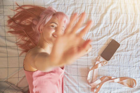 Playful woman hides from camera closing lens by palm on comfortable bedの写真素材