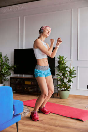 Beautiful woman in tracksuit with headphones dances in living roomの写真素材