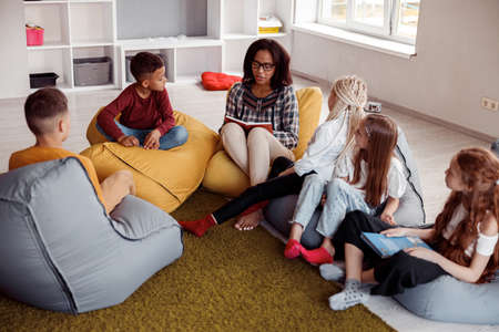 Teacher sitting on a pouf and reading for schoolchildrenの写真素材