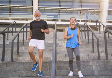 Active mature couple, man and woman in sportswear training together outdoors on the stairs in city to stay fitの写真素材