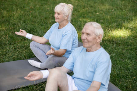 Cheerful senior woman and man meditates sitting in lotus poses on lawn grassの写真素材