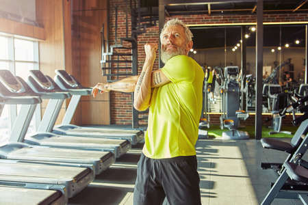 Portrait of athletic middle aged man in sportswear doing stretching exercises, warming up before workout in a gym or sport clubの写真素材