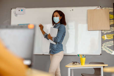 Young teacher in a mask standing in the classroomの写真素材