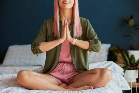 Smiling female model meditates holding hands in namaste mudra on large bed closeupの写真素材
