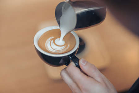 Female hands decorating coffee with milk and making latte artの写真素材