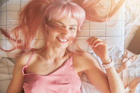 Pretty lady with colorful hair on face smiles lying on bed with checkered linenの写真素材