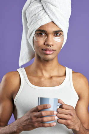Close up portrait of young man with eye collagen patches in shower towel on headの写真素材